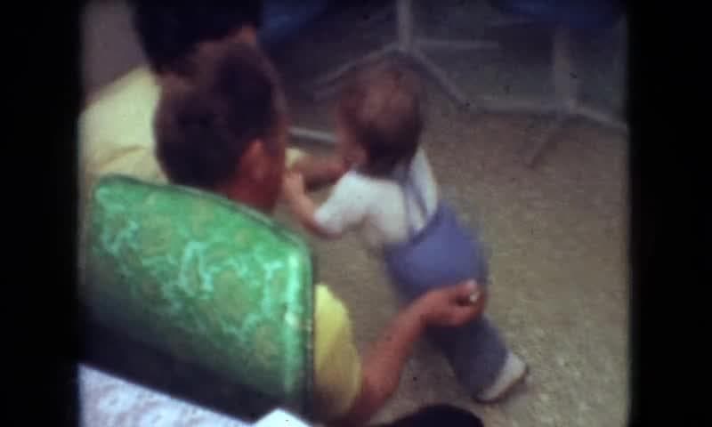 1966: Athens Ohio, USA. A Small Child Standing Next To A Man On A Couch.