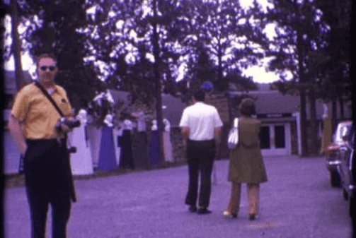 1974 South Dakota people walking and man in yellow shirt with camera.