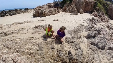 Two Children Sitting On The Rocks On The Beach