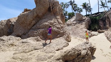 Two People Walking On The Beach Near The Rocks
