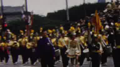 California USA (1961): Marching Band Going Down The City Streets Entertaining A