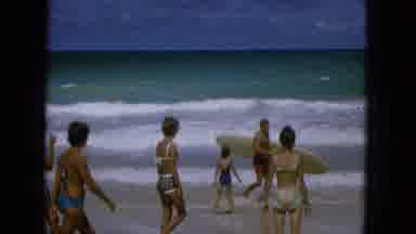 1965: Beachgoers in 1960s Bikinis Walking with Surfboard on Molokai Shore