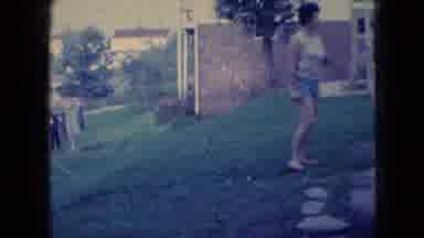 Wellsburg Iowa (1965): Man Outside Smoking Cigarette While Wife And Child Play
