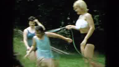 Wellsburg Iowa (1965): Mother Spraying Her Kids With A Water Hose For Fun Outdoors