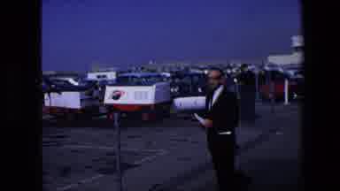 AMSTERDAM NETHERLANDS-1967: Reporter In Suit Speaking In Parking Lot Near NASA Vehicles