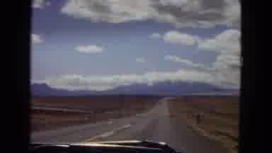 Arizona (1967): Cars Drive Down A Rural Highway With Mountains Off In The Distance