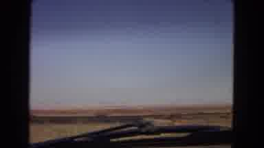 Arizona (1967): A Moving Vehicle Passes Road Signs In A Rural Area And A Building