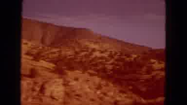 Arizona (1967): Driving Down Road With Small Hills On Roadside During Sunny Day