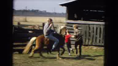 Arizona (1967): Man Riding A Smaller House Across A Backyard Showing A Family