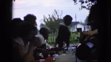 California USA (1969): Family Sharing Meal Outside While Matriarch Performing
