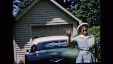 California USA (1969): An Elderly Woman Stands In A Home's Driveway And Waves