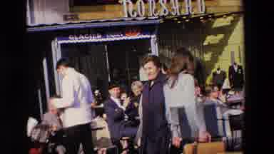 Loudes France (1969): Man Waves At Passers While Sitting At An Outdoor Cafe