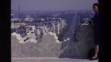 Loudes France (1969): Woman Posing On A Tall Wall In Front Of A City
