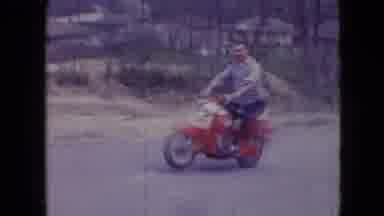 Athens Ohio USA (1966): Man Riding On Red Scooter Does A Small Wheelie And Smiles