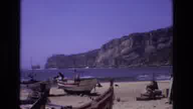 PORTUGAL-1972: Blonde Woman Walking On Beach Near Cliffs Surrounded By Small Boats