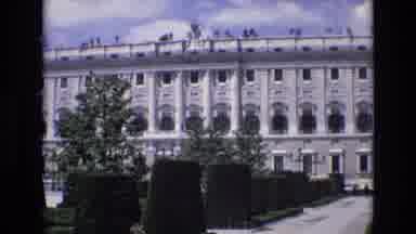 Spain (1972): People Stroll On A Walkway Lined With Trees Near A Large Building