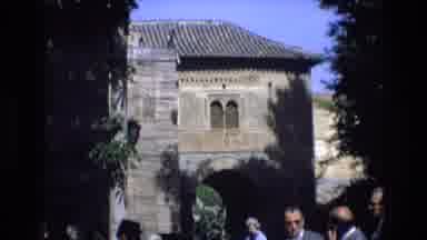 Spain (1972): People Standing Outside Brown Brick Building