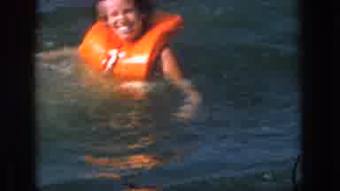 Michigan USA (1961): Smiling Woman Floating In Orange Life Vest Followed By Boy