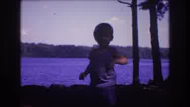 Baxter Maine USA (1975): Small Boy Eating A Snack On A Shoreline Of A Lake