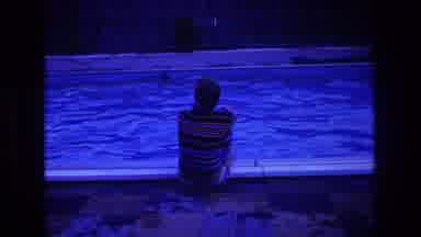 Boston USA (1975): Man Dressed In Striped Shirt Sitting On Edge Of Pool Looking