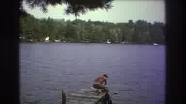 Boston USA (1975): View Of Lake With A Man On Pier With Moving And Docked Boats