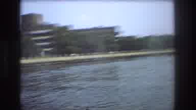 Boston USA (1975): A Large Multi-Story Building Sits Behind Trees On The Bank Of A