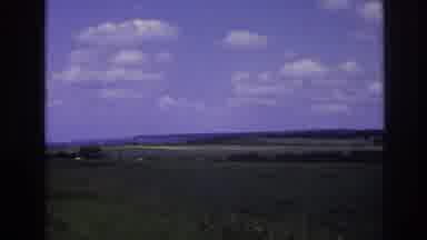 France (1967): A Vehicle Travels Down A Paved Road Cutting Through A Green Field