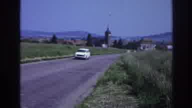 France (1967): White Vehicle Driving Away From Town On Open Road Daytime