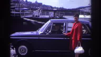 France (1967): Red Coated Lady Poses Beside Male Driver In The Forefront Of A