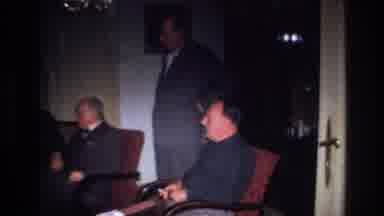 France (1967): Men In Suits Sitting In Chairs As A Group In A Dark Room Together