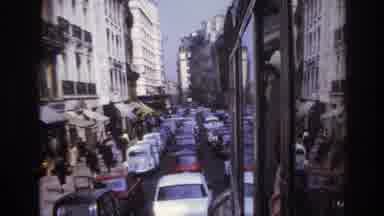 Paris France (1967): Cars Driving Alongside Pedestrians Down A Street Surrounded
