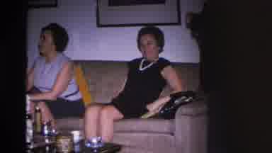 Hoboken New Jersey USA (1966): Woman Sitting On Couch While Man Holds Bottle Of