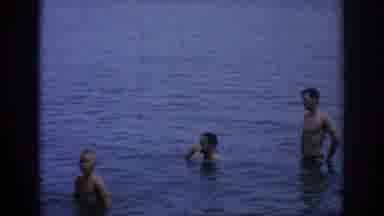 Oklahoma USA (1967): A Man Starting A Fire While Other Men And Children Swim In A