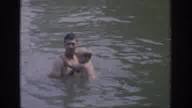Oklahoma USA (1967): Boy Climbing On Dad Looking Scared Of Water When They Are