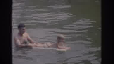 Oklahoma USA (1967): Man Floats Boy On Board In Lake As Waves Pass While Smiling