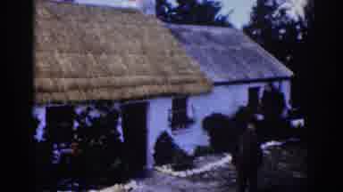 Dublin Ireland (1961): Priest With Camera Walks Toward House With Thatched Roof