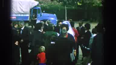 Spain (1966): Small Crowd Of People Dressed In Black Crowd Near A Blue Truck After