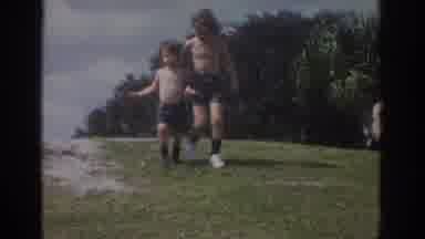 Miami Florida USA (1971): Tow Shirtless Kids Running Down A Hill Past Some Adults