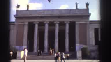 Greece (1976): A Building With Corinthian Columns And People Walking Down Its