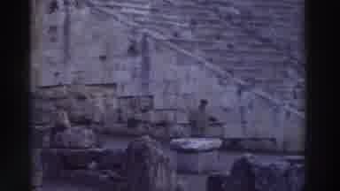 Greece (1976): Man In Heavy Coat Waving At Himself As He Enters Ancient Roman