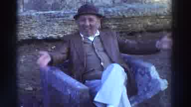 GREECE-1976: Older Man Waving on Stone Bench, Ferry in Harbor
