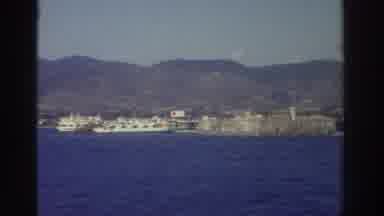Greece (1976): A Shoreline Is Seen From A Ship And Other Boats Are At A Pier