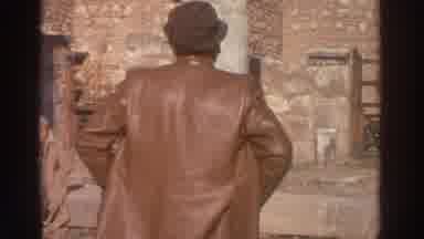 Greece (1976): A Man In A Leather Jacket Studies An Old Structure While A Woman