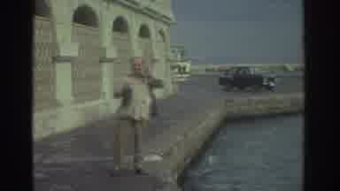 Greece (1976): Man Standing At Water's Edge On A Windy Day As Fisherman Tries His