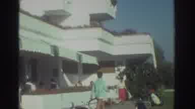 Greece (1976): People Strolling Near White Building With Plants Balconies On Clear
