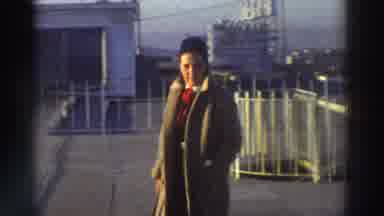 Greece (1976): A Guy In A Brown Overcoat Is Walking On A Roof Near The Rail