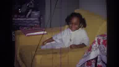 Harlem New York USA (1976): A Black Girl Sits In A Yellow Chair And Smiles While A