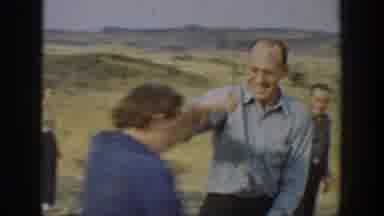 California USA (1937): Two Men Saw Wood While Small Crowd Gathers At Field