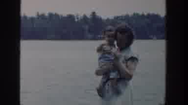 Wisconsin USA (1953): A Smiling Mom Holding A Baby While Walking In Front Of A