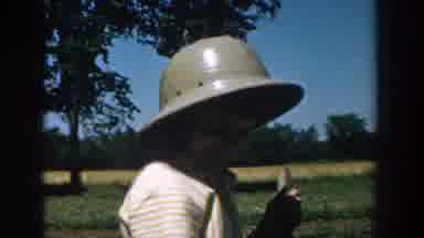 Michigan USA (1957): Woman Wearing Hat And White Shirt Doing Yard Work On Sunny